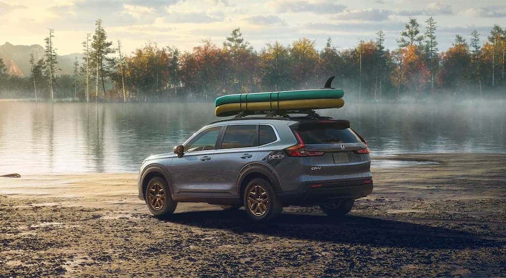 Blue 2023 Honda CR-V with paddleboards strapped to the roof parked near a lake