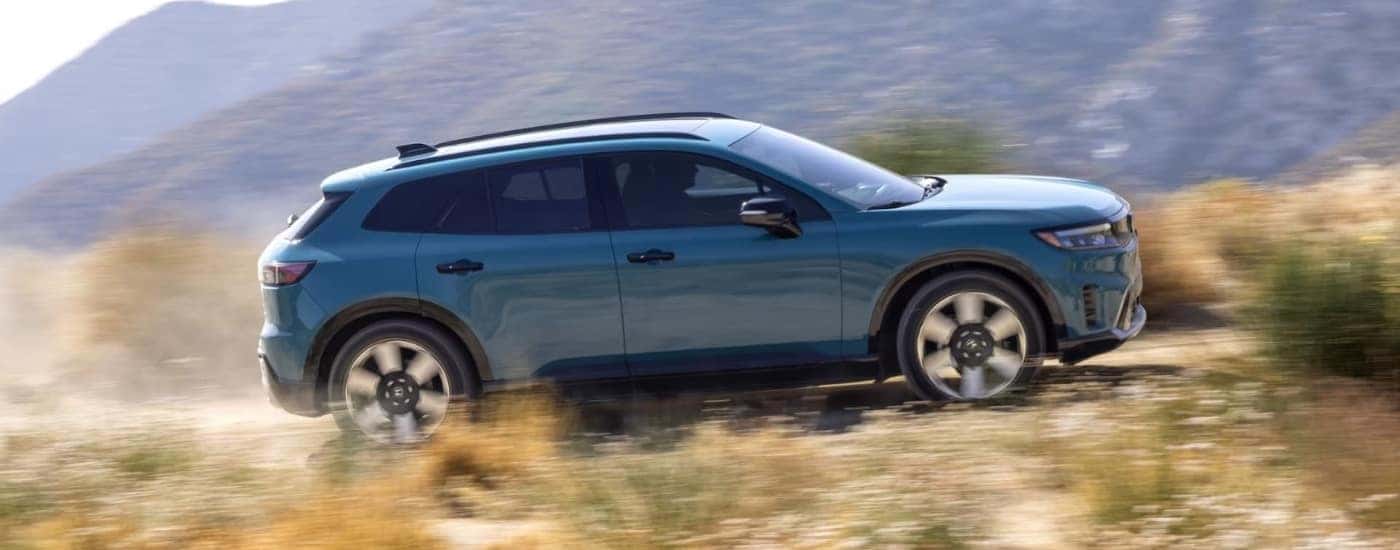 Blue 2024 Honda Prologue Elite driving by a mountain.
