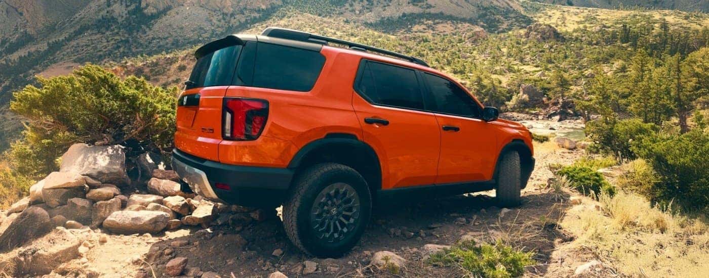 Orange 2026 Honda Passport driving off-road from the rear