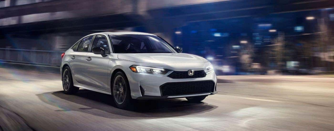Silver 2026 Honda Civic Hybrid Sport driving at night with a city in the background