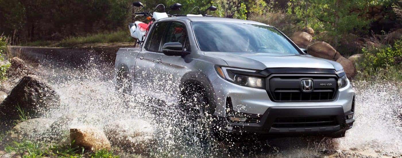 Silver 2026 Honda Ridgeline Sport driving through a river with a dirt bike in the back