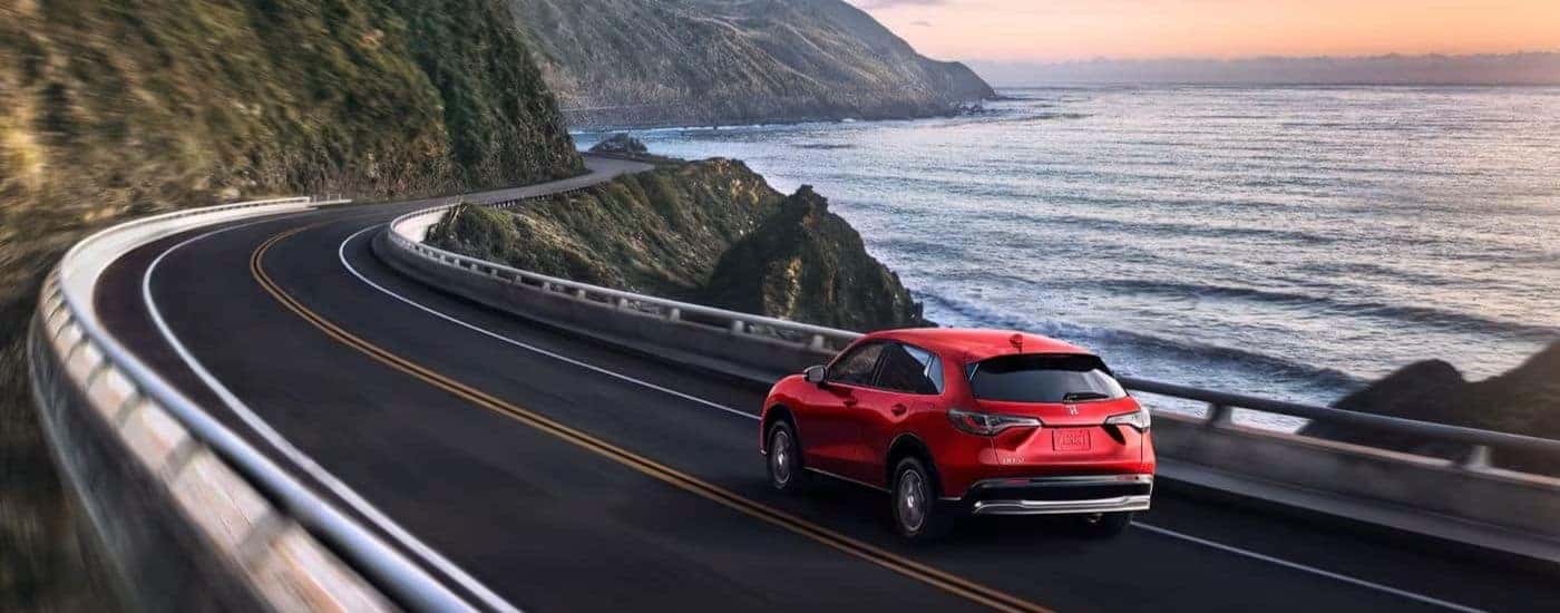 Red 2023 Honda HR-V EX-L driving by water.