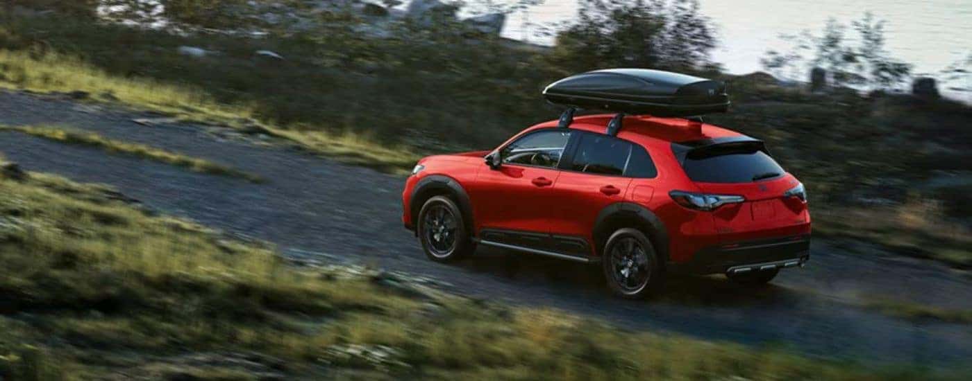 Red 2026 Honda HR-V Sport driving on a dirt road with a roof box