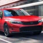 Red 2026 Honda Civic driving down a city street.