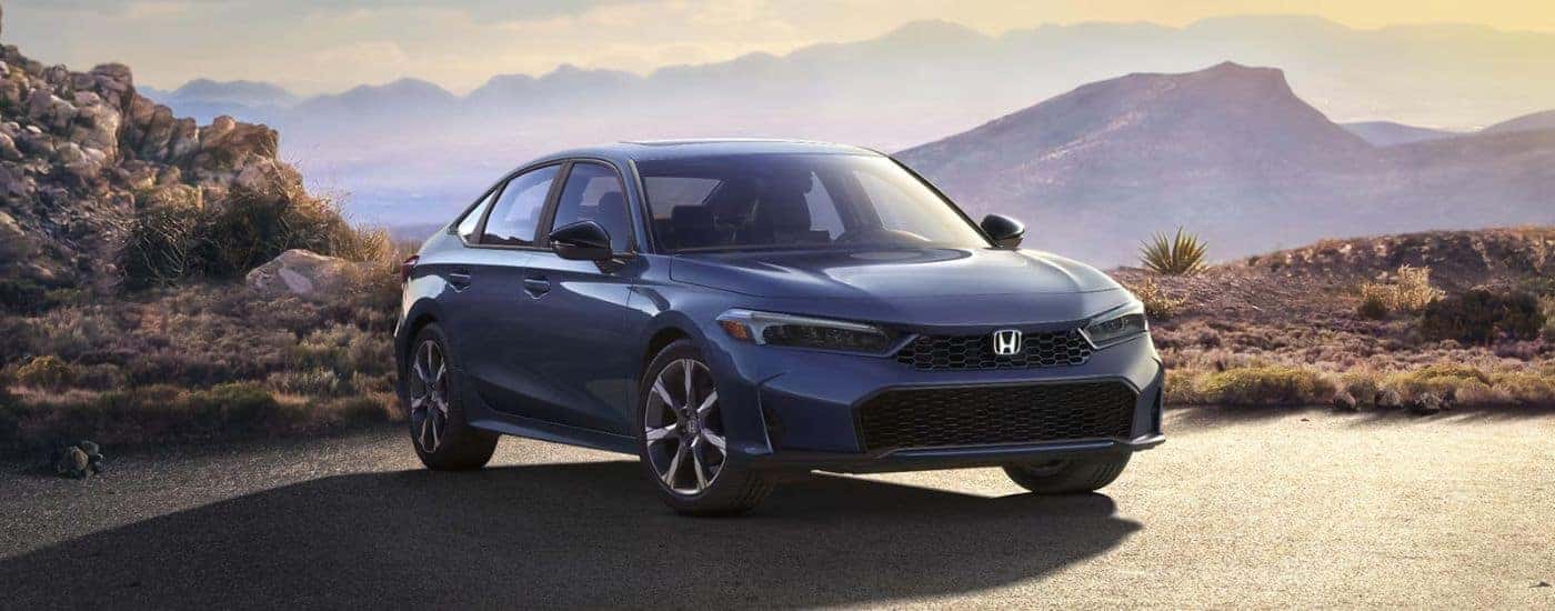 A blue 2026 Honda Civic Sport Touring Hybrid parked in front of mountains.