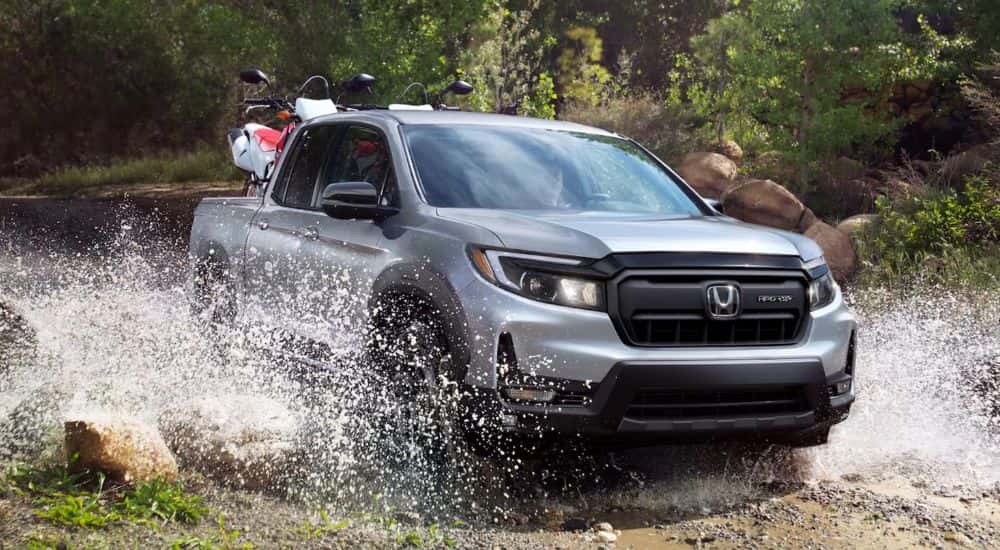 A silver 2026 Honda Ridgeline shown driving through a puddle.