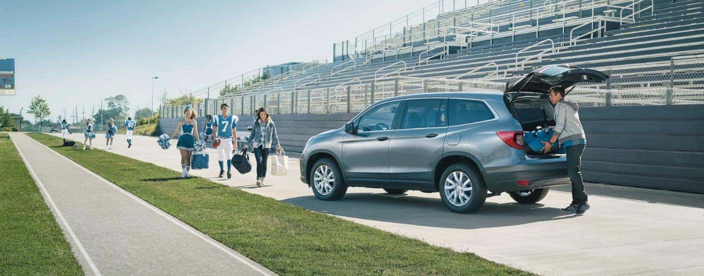A silver 2021 Honda Pilot parked by bleachers at a football game.