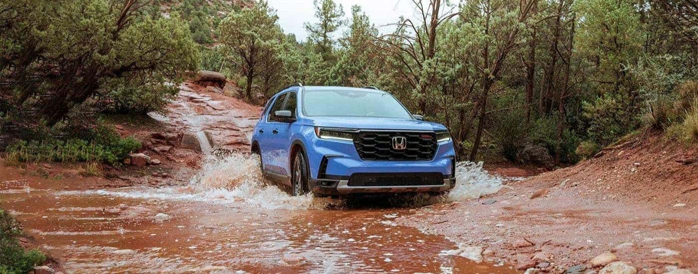 A blue 2023 Honda Pilot TrailSport driving through mud.