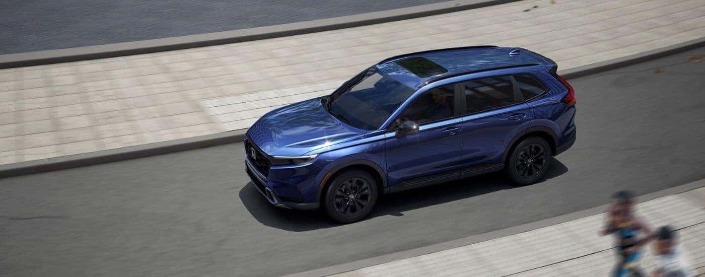 Blue 2026 Honda CR-V Hybrid aerial view driving on the road.
