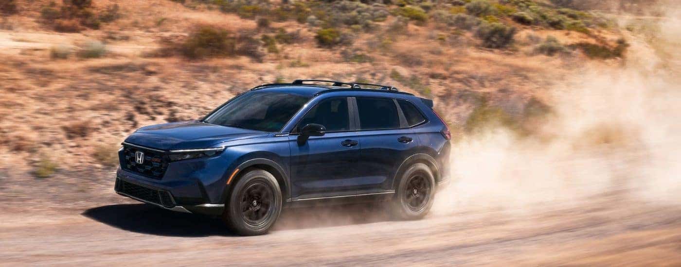 Blue 2026 Honda CR-V Hybrid driving on a dusty trail.