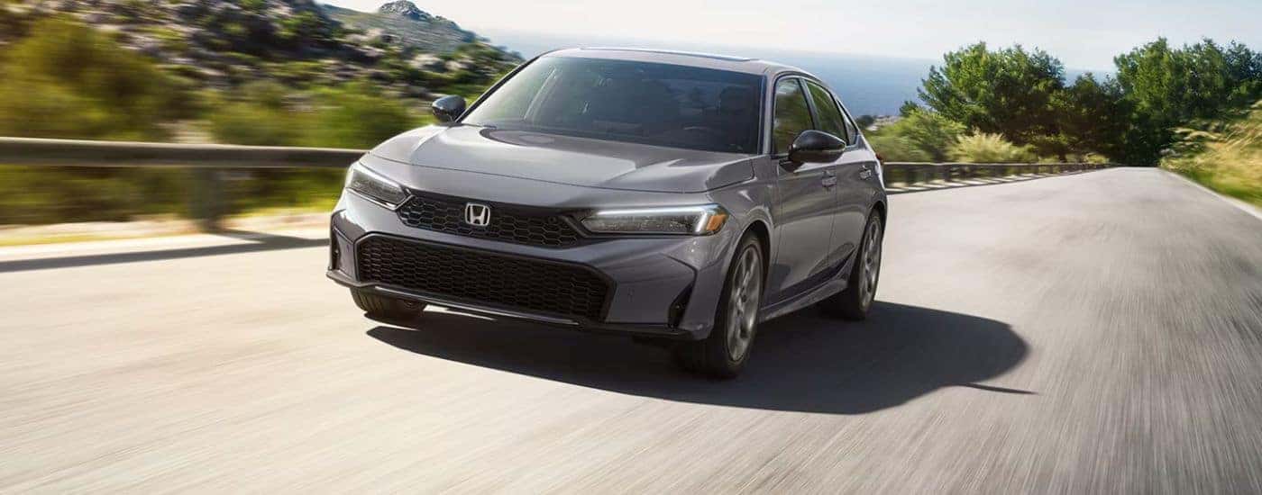 Grey 2026 Honda Civic driving on a road near a body of water.