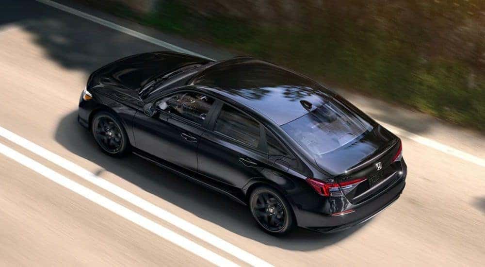 Black 2026 Honda Civic Sport driving down a road.