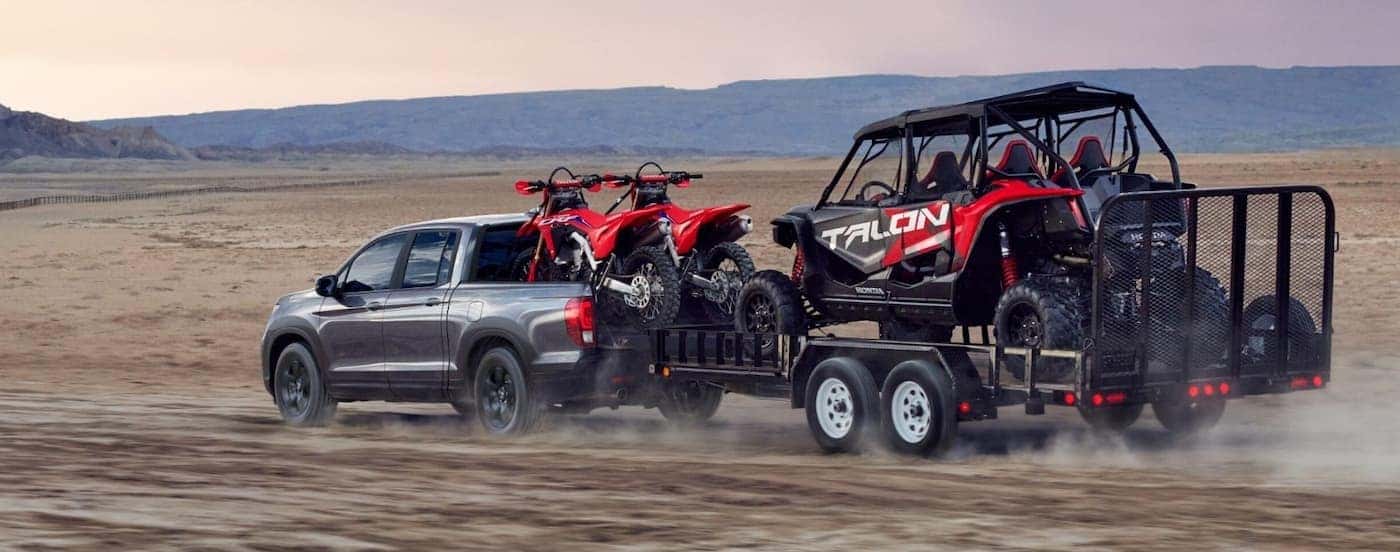 A silver 2026 Honda Ridgeline TrailSport towing a trailer offroad.