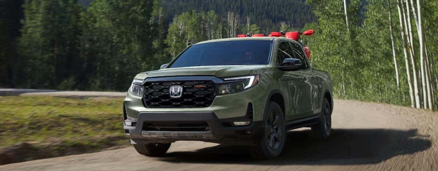 A green 2026 Honda Ridgeline TrailSport driving on a dirt road.