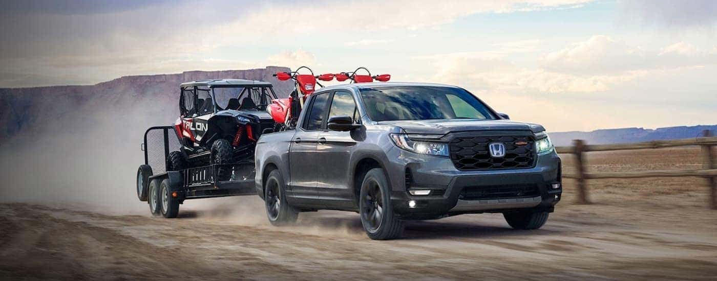 A silver 2026 Honda Ridgeline TrailSport towing a trailer offroad.