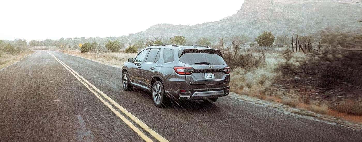Rear view of a grey 2023 Honda Pilot Elite driving on a paved road.