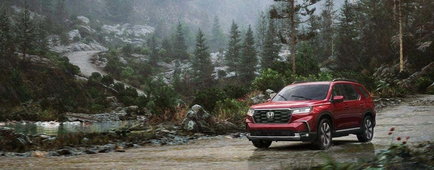 Red 2023 Honda Pilot Elite parked off-road in the woods.