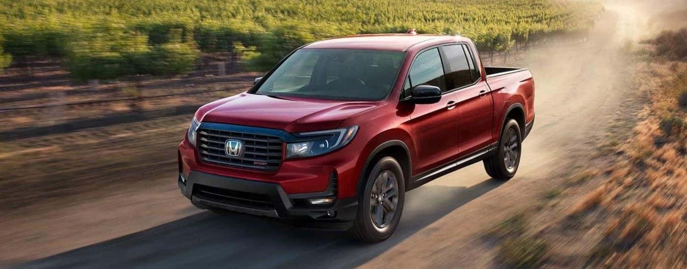 A red 2023 Honda Ridgeline Sport driving off-road.