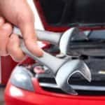 hand holding tools in front of car with hood open to perform car service.