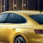 A man and woman leaving a coffee shop to get into a 2019 Volkswagen Arteon in gold.