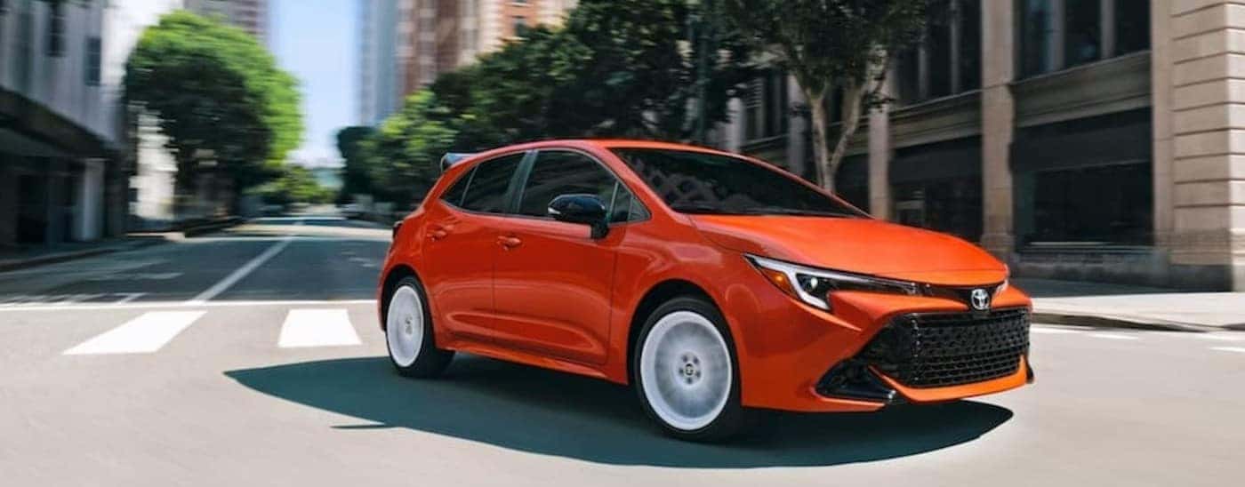An orange 2026 Toyota Corolla hatchback driving in a city.